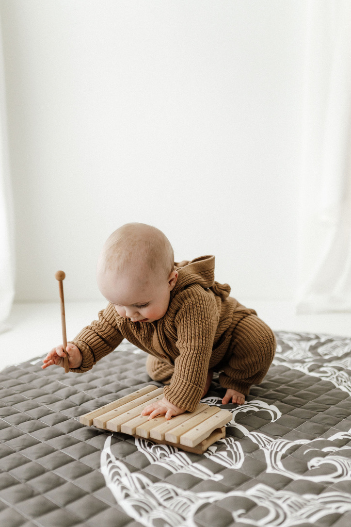 baby happily playing on a playmat with Māori designs