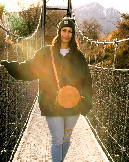 Woman standing on a suspension bridge wearing a tan crossbody bag