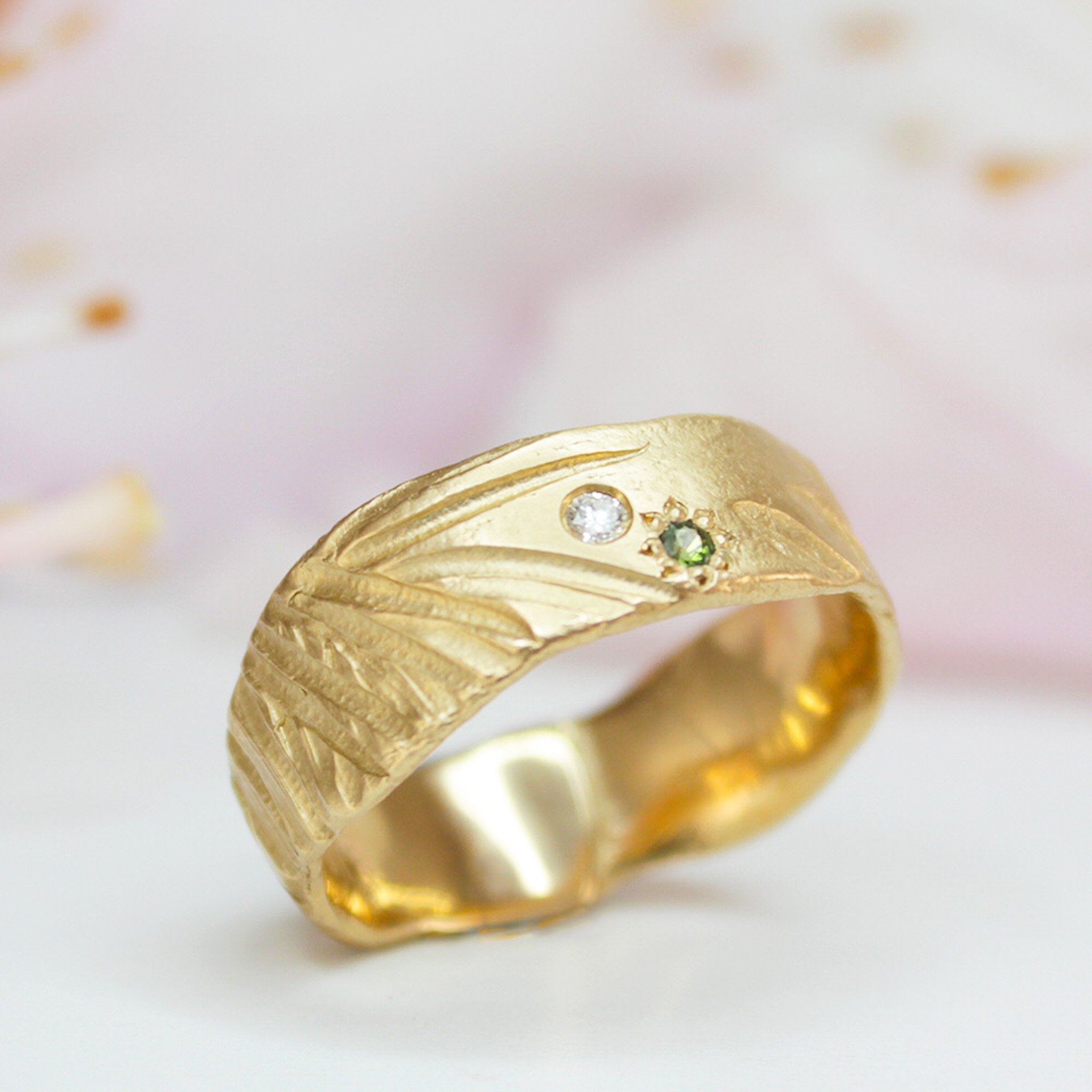 Gold band ring with a round diamond and green jewel 