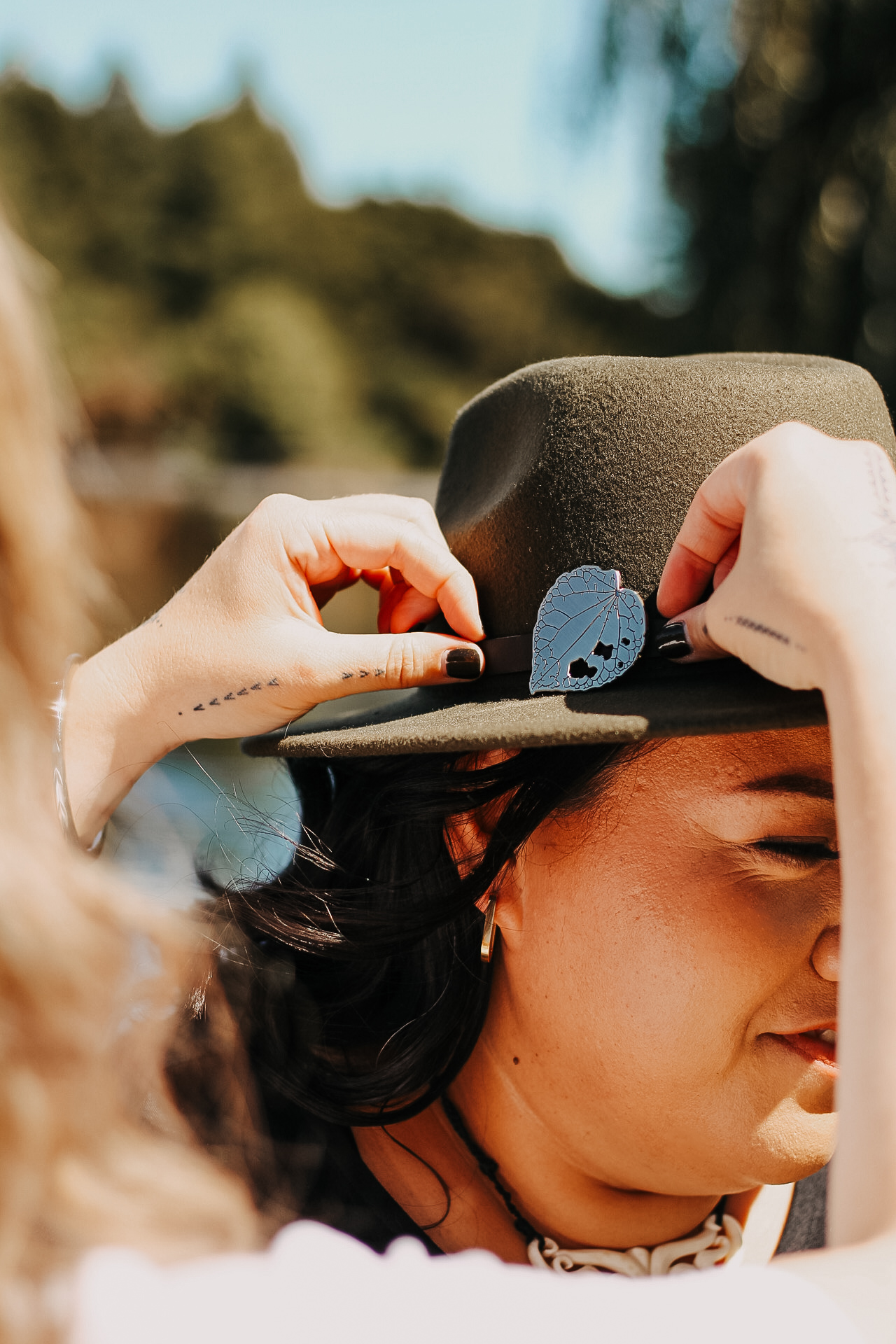 Woman wearing a olive hat with silver kawakawa brooch