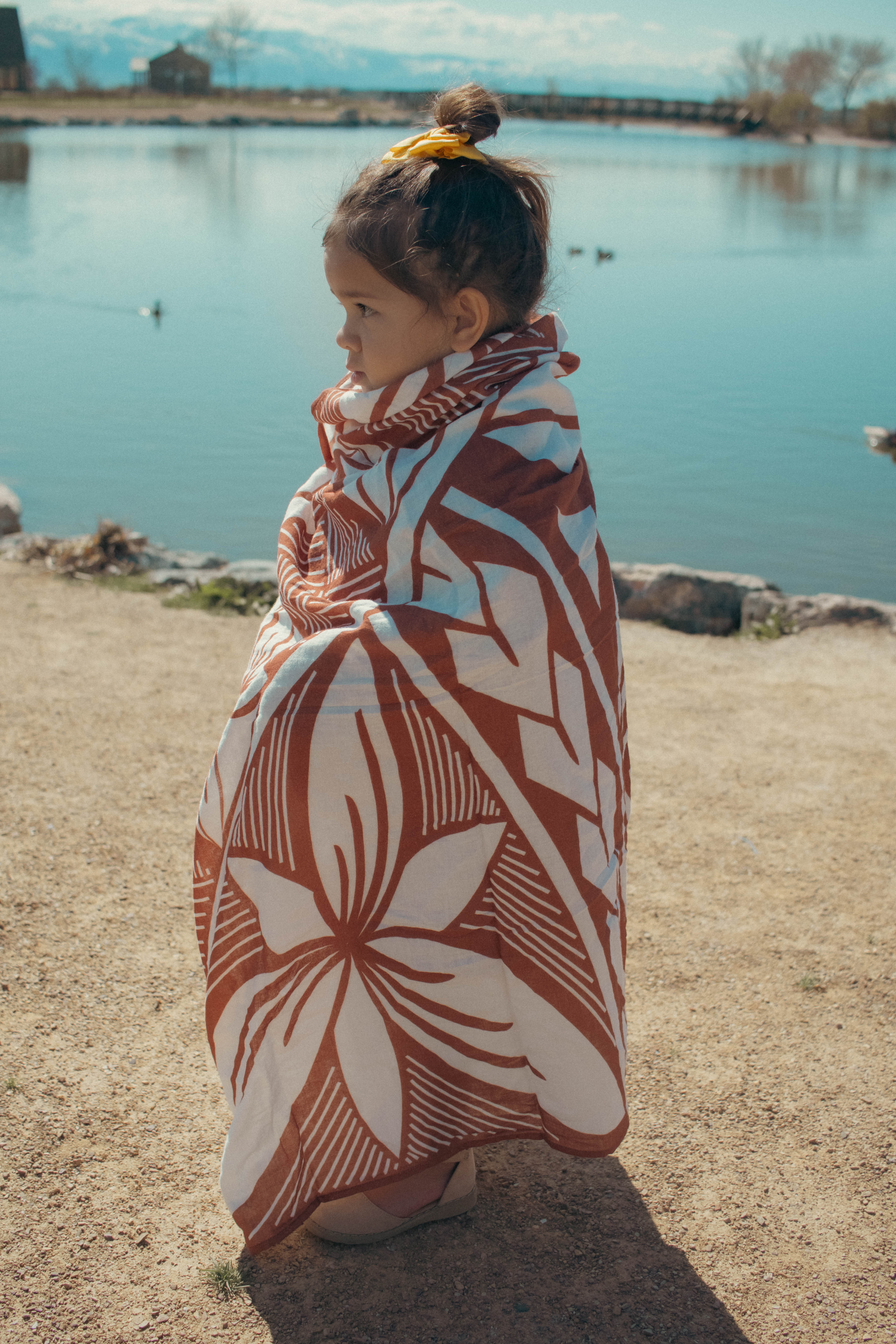 Young girl wrapped in a rust coloured polynesian inspired baby blanket