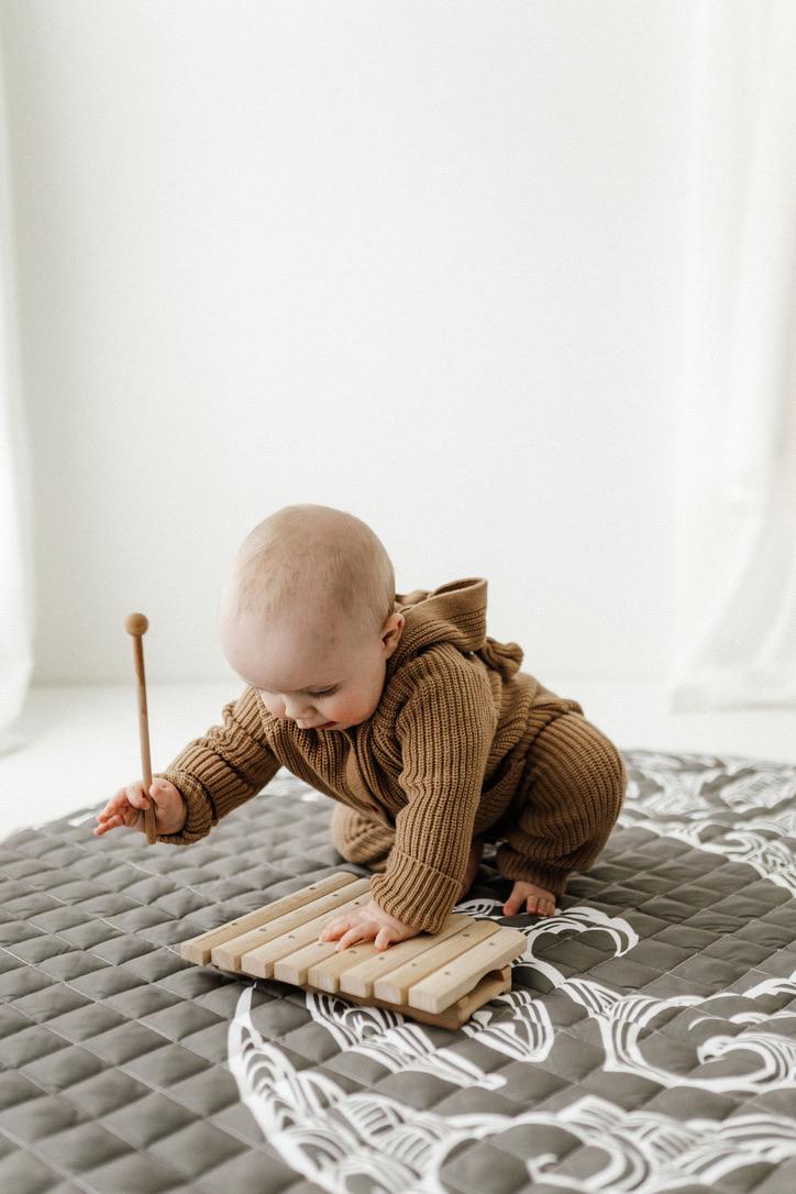 baby happily playing on a playmat with Māori designs