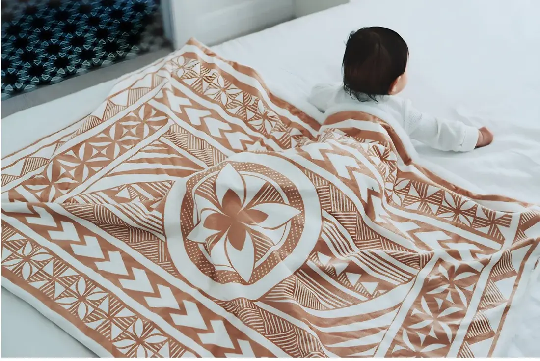 Baby laying underneath a polynesian inspired baby blanket