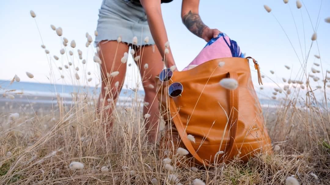 Woman at beach grabbing things out of her tan leather beach bag