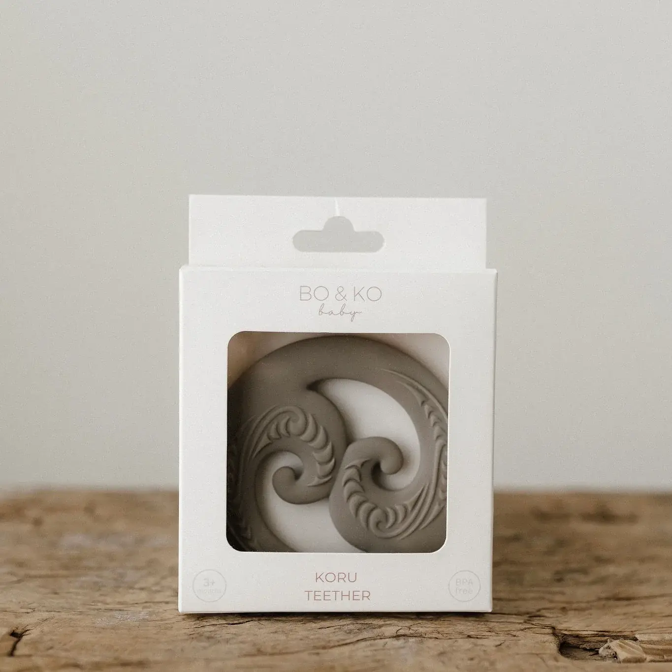 Maori inspired baby teether in white box on a wooden stool