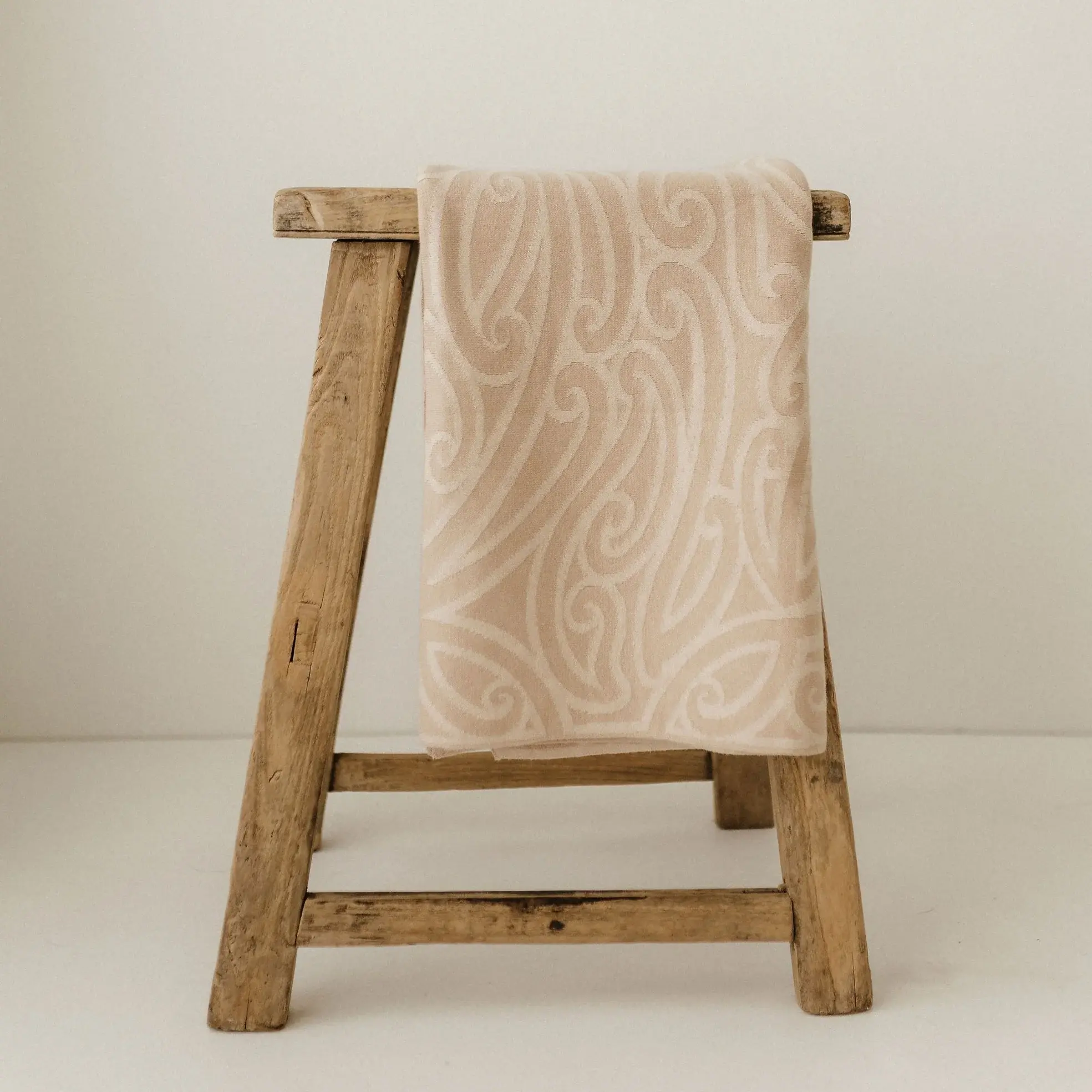 Maori inspired babyb blanket draped over a rustic wooden stool