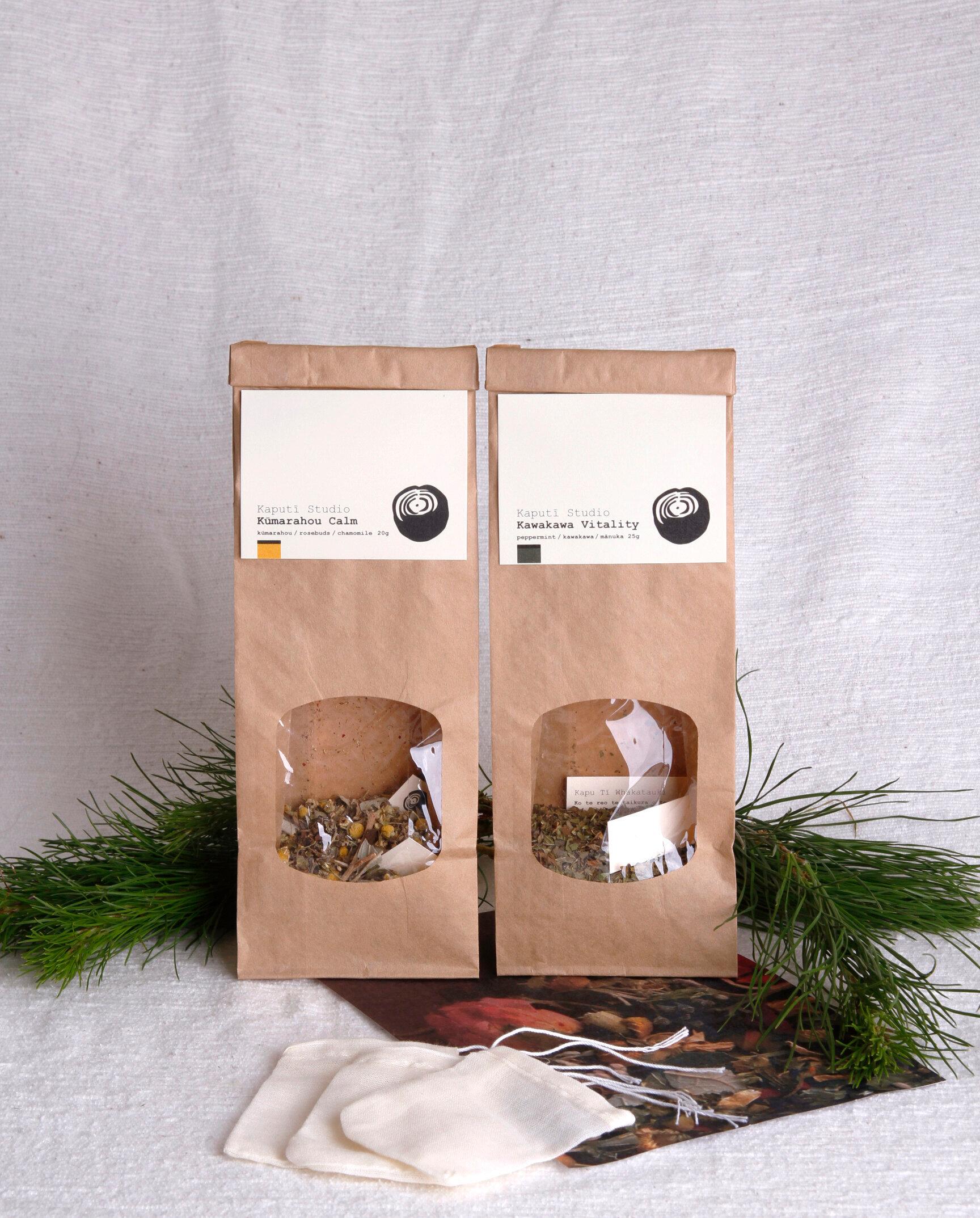 Two brown bags of loose leaf tea next to greenery and a white linen background